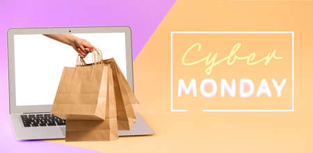 Woman sticking hand with shopping bags out of laptop screen on color background. Cyber Monday Saleの写真素材
