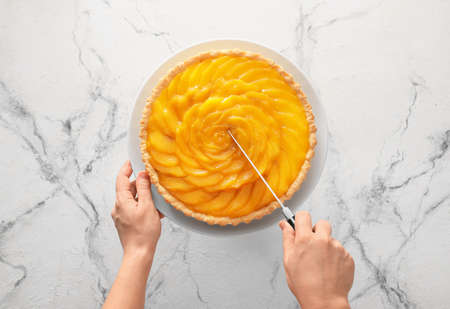 Woman cutting tasty mango pie on light backgroundの写真素材