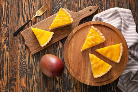 Board with pieces of tasty mango pie on wooden backgroundの写真素材
