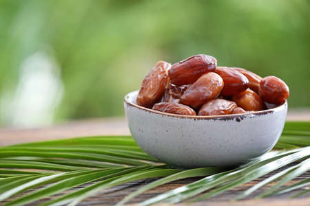 Bowl with sweet dried dates on table against blurred background