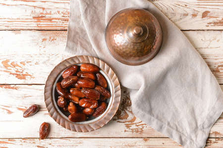 Plate with sweet dried dates on light wooden background