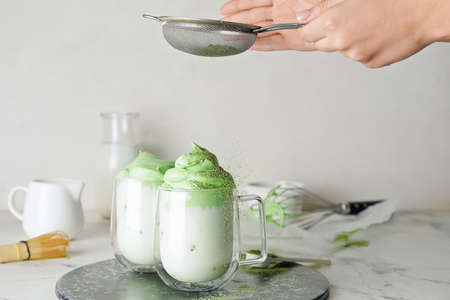 Woman preparing tasty dalgona matcha latte on light backgroundの写真素材