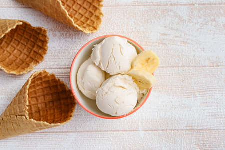 Tasty banana ice cream and waffle cones on light wooden backgroundの写真素材