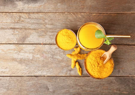 Glass of healthy turmeric drink and bowls with powder on wooden background
