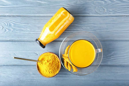 Cup and bottle of healthy turmeric drink on color wooden background