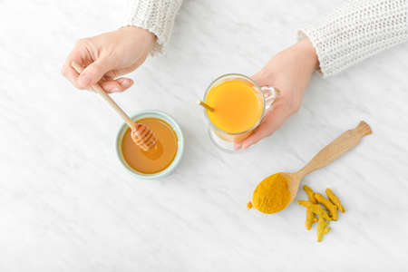 Woman making healthy turmeric drink with honey on light backgroundの写真素材