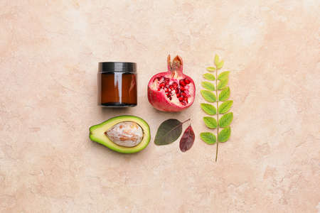Composition with jar of natural cream, avocado and pomegranate on color background