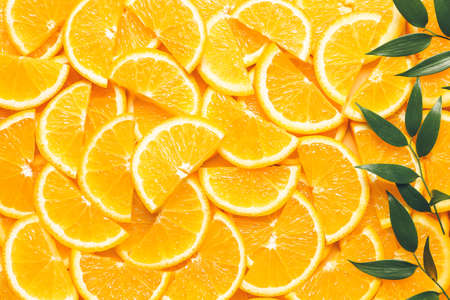 Pieces of fresh oranges with green leaves as backgroundの写真素材