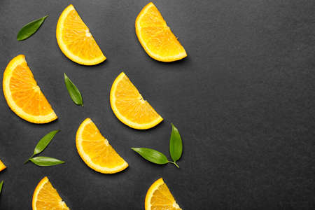 Slices of fresh oranges with green leaves on dark background