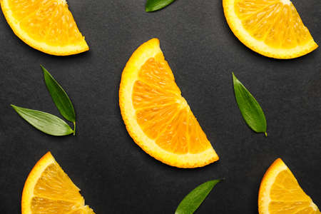 Slices of fresh oranges with green leaves on dark background