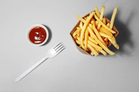Box with tasty french fries, fork and sauce on light backgroundの写真素材