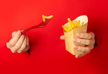 Creative composition with female hands and box of tasty french fries on color backgroundの写真素材
