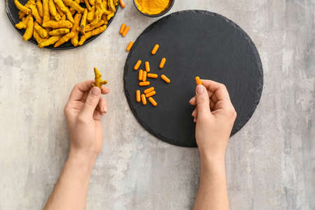 Woman holding turmeric pill and root on grunge backgroundの写真素材