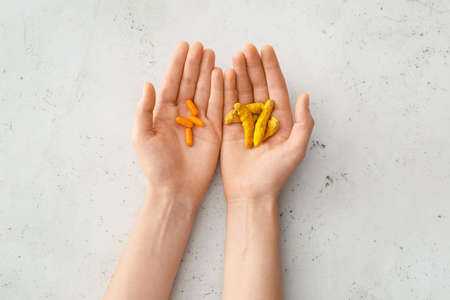 Female hands with turmeric pills and roots on light backgroundの写真素材