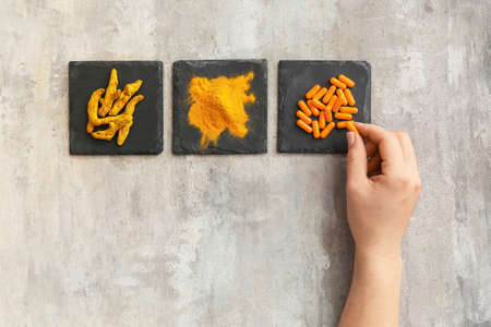 Female hand with turmeric pills, roots and powder on grunge backgroundの写真素材
