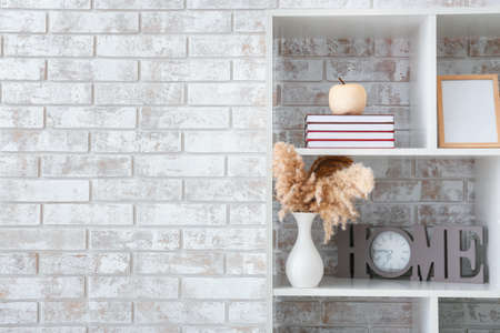 Books, frame and decor on shelf near brick wallの写真素材