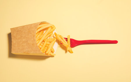 Box with tasty french fries and fork on color backgroundの写真素材