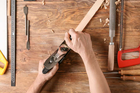 Carpenter planing plank on wooden backgroundの写真素材