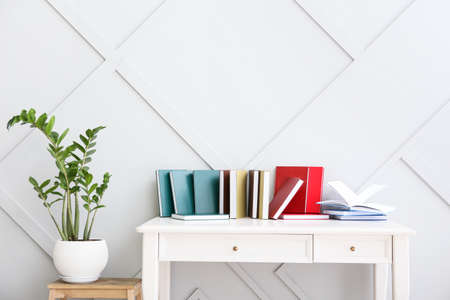 Table with different books and houseplant near light wallの写真素材