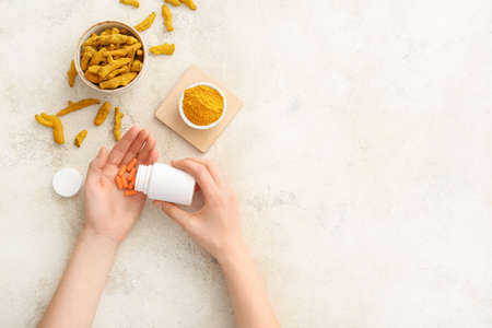 Female hands with turmeric pills, powder and roots on light backgroundの写真素材