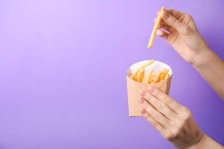 Woman eating tasty french fries on color backgroundの写真素材