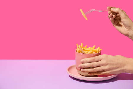 Female hands and cup with tasty french fries on color background