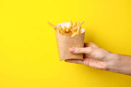 Female hand and box with tasty french fries on color backgroundの写真素材