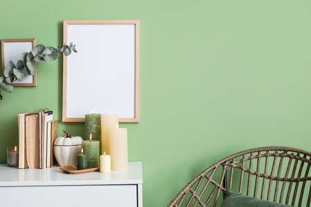 Burning candles and books on chest of drawers near color wallの写真素材