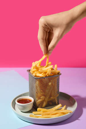 Female hand with tasty french fries on color backgroundの写真素材