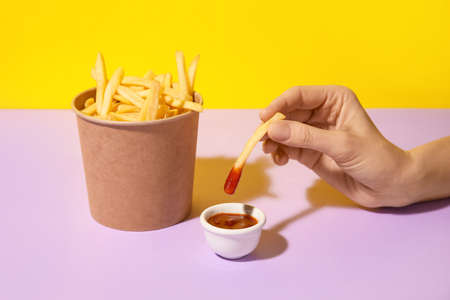 Woman eating tasty french fries with sauce on color backgroundの写真素材