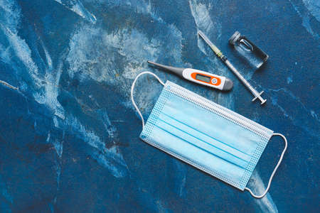 Electronic thermometer with medical mask, vaccine and syringe on color background