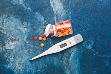 Electronic thermometer with pills on color background