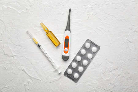 Electronic thermometer with pills, vaccine and syringe on white background