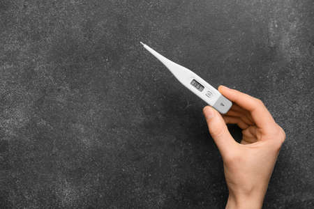 Female hand with electronic thermometer on dark background