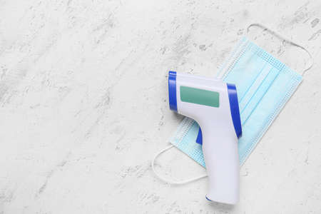 Infrared thermometer with medical mask on white backgroundの写真素材