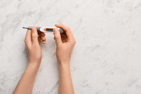 Female hands with electronic thermometer on white backgroundの写真素材