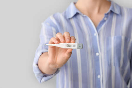 Woman with electronic thermometer on gray background, closeupの写真素材