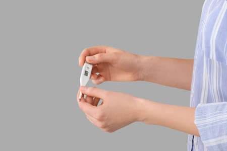 Woman with electronic thermometer on gray background, closeupの写真素材