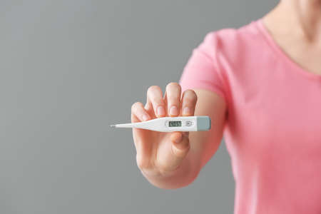 Woman with electronic thermometer on gray background, closeupの写真素材