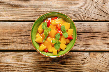 Bowl with tasty mango salad and sauce on wooden backgroundの写真素材