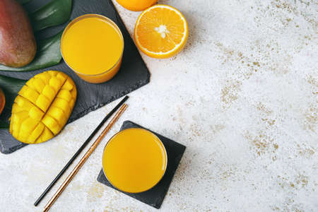 Glasses of mango juice and tropical fruits on light backgroundの写真素材