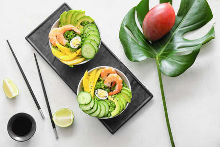 Bowls of fresh salad with mango, shrimps and vegetables on light backgroundの写真素材