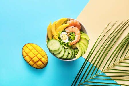 Bowl of fresh salad with mango, shrimps and vegetables on color background
