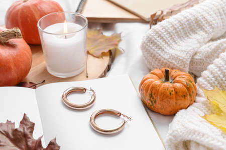 Beautiful autumn composition with book, female jewelry and aroma candle on bedの写真素材