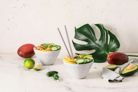 Bowls of fresh salad with mango, shrimps and vegetables on light background
