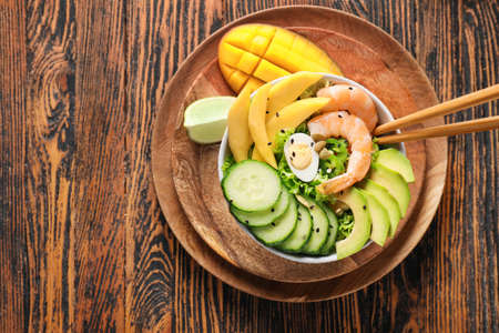 Bowl of fresh salad with mango, shrimps and vegetables on wooden backgroundの写真素材