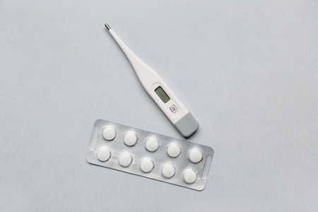 Thermometer and pills on light background