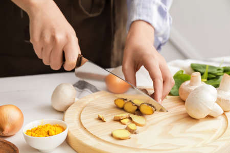 Woman cutting ginger on table in kitchen
