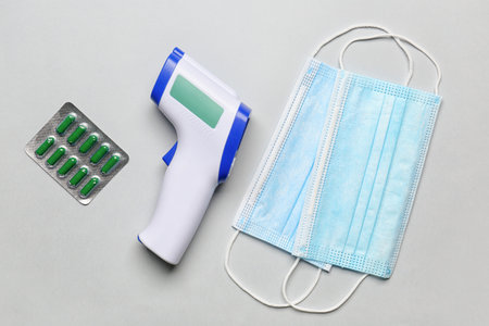 Infrared thermometer, masks and pills on light background