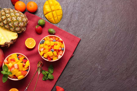 Bowls with salad and tropical fruits on dark background